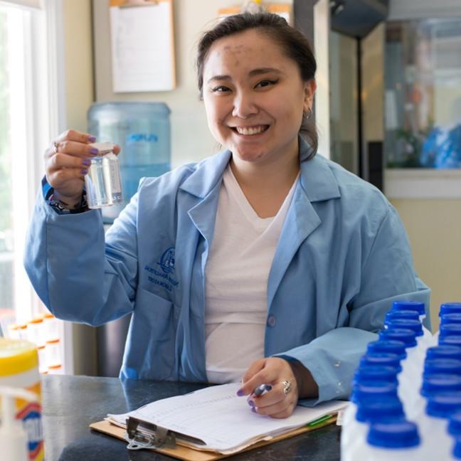 A student smiles as they hold up a small bottle of clear liquid